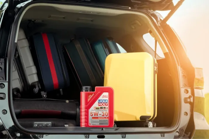 Rote Flasche Liqui Moly 5W-30 Nachfüll-Öl im vollgepackten Kofferraum eines Autos neben gelben und blauen Koffern.